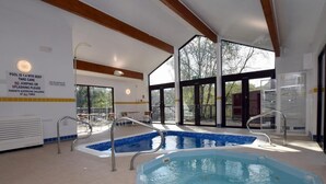 Una piscina interior con señalización de seguridad clara, una zona soleada con mesas y sillas, y amplios ventanales que ofrecen vistas al exterior.