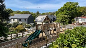 Un parque infantil con tobogán y estructura de escalada, rodeado de edificios residenciales y áreas verdes.