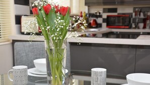 Una mesa de comedor con un florero de vidrio, platos blancos y tazas estampadas.