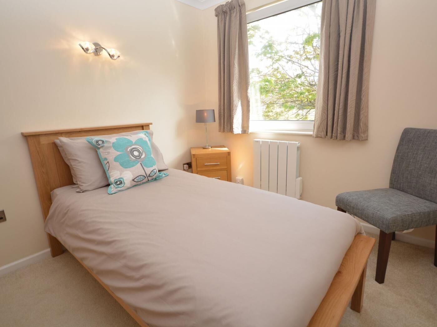 A bedroom with a bed, a chair, a bedside table, a lamp, and a window with curtains.