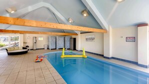 Una piscina interna con soffitto in legno, una poltrona e un cartello con le regole della piscina.