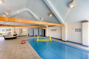 Ein Innenpool mit Holzbalkendecke, einer Sitzecke und einem Hinweisschild zu den Poolregeln.