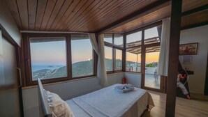 Une chambre avec un lit, de grandes fenêtres, une vue sur le paysage et un tableau au mur.