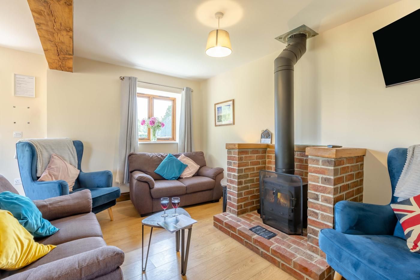 A cozy living room with a fireplace, sofas, a table with glasses, and a window with curtains.