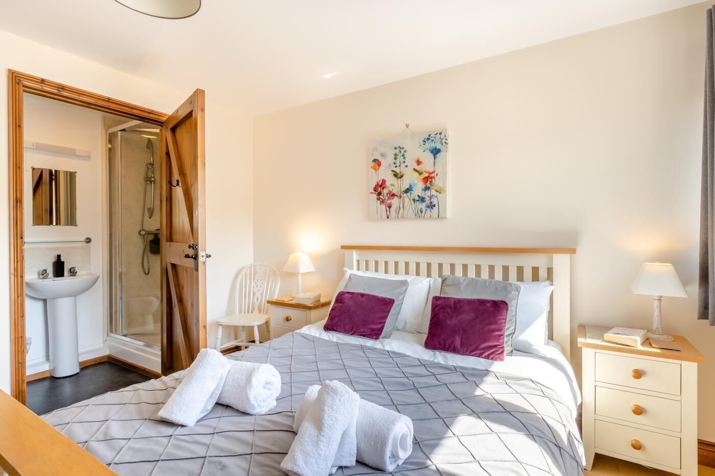 Quarto com cama, mesas de cabeceira, apoio para luminária, cadeira, chuveiro e pia.