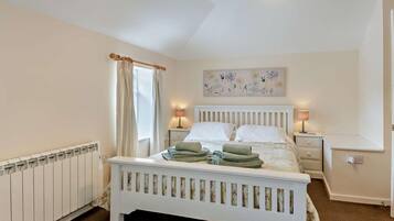 A bedroom with a white bed, two bedside lamps, a radiator, and a window with curtains.