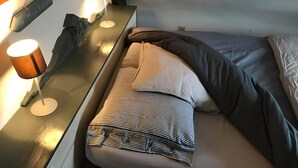A bed with a striped pillow, a bedside table with a lamp, and a wall-mounted sign. - Gîte La Chaumière de Claire - Anouck (Saint-André-des-Eaux)
