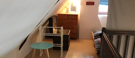 Une chambre à coucher aménagée dans un espace de type « loft », avec un plancher en bois, une petite table, une chaise, un lit, une commode et un escalier.