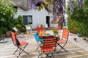 A wooden deck with outdoor seating, a thatched-roof building, and lush greenery.