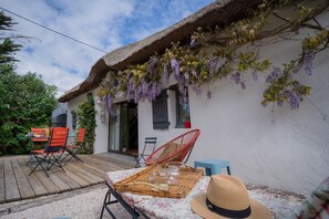 Ein rustikales Haus mit einem Strohdach, Sitzgelegenheiten im Freien und hängenden violetten Blüten.