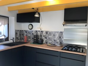 A modern kitchen with a gas stove, a coffee maker, and a clock on the wall.