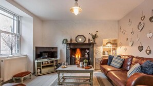 Una sala de estar acogedora con chimenea, sofá de cuero, televisor y estantería.