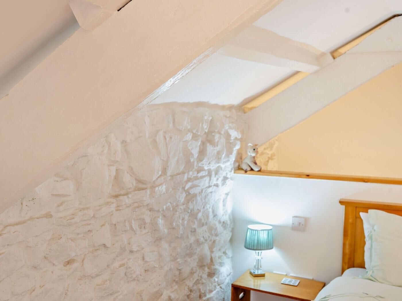 Ein Schlafzimmer mit schrägen Wänden, einem Holzkopfende, einer Nachttischlampe und einem kleinen Nachttisch.