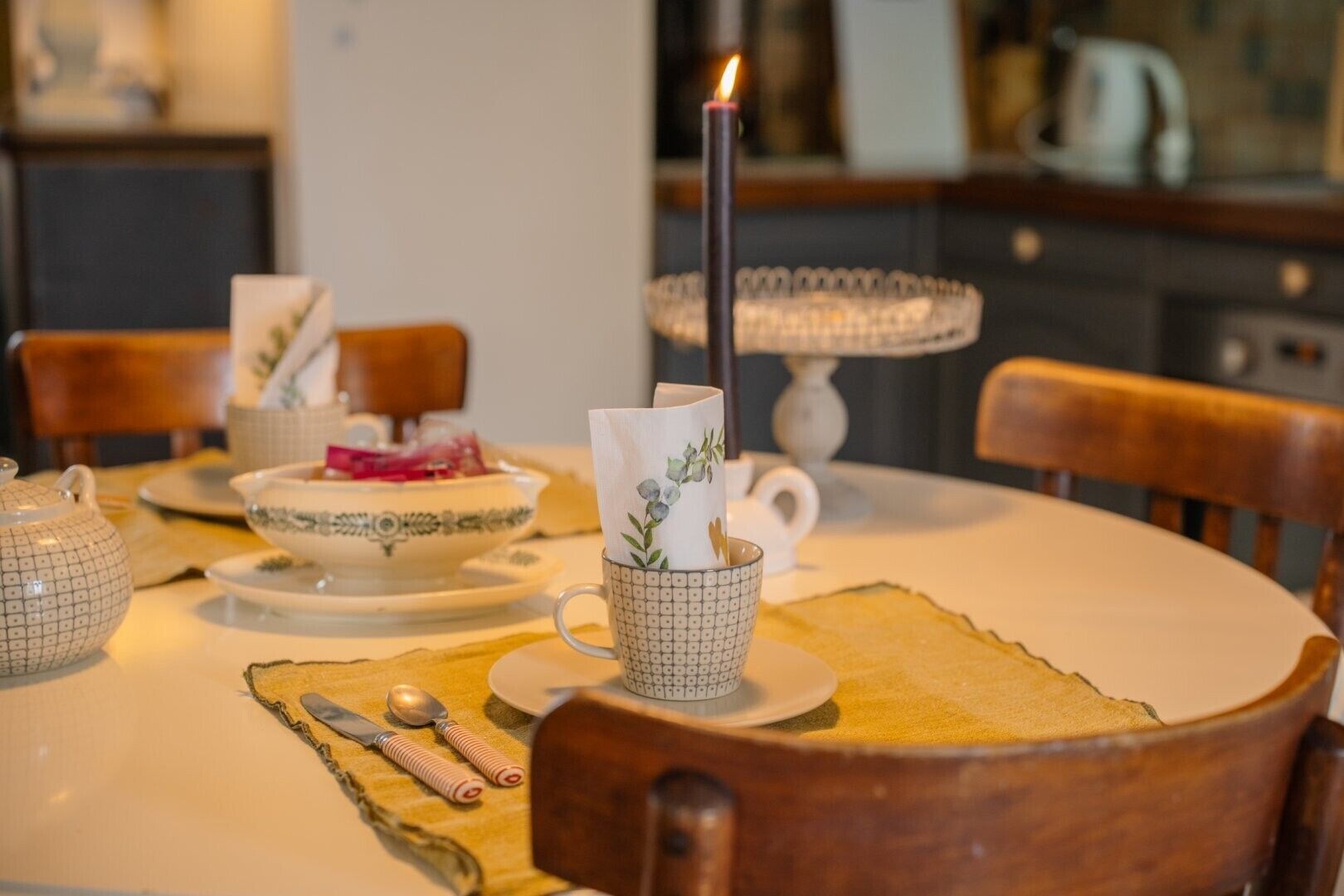 Una mesa de comedor con una tetera, tazas y una vela.