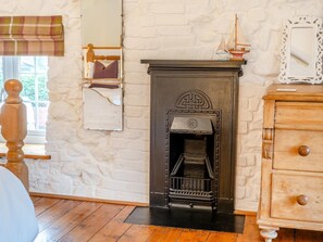 A room with a fireplace, a wooden dresser, a plaid window valance, and a stone wall. - 1 Bed in Kidwelly (oc-43409) (Kidwelly)