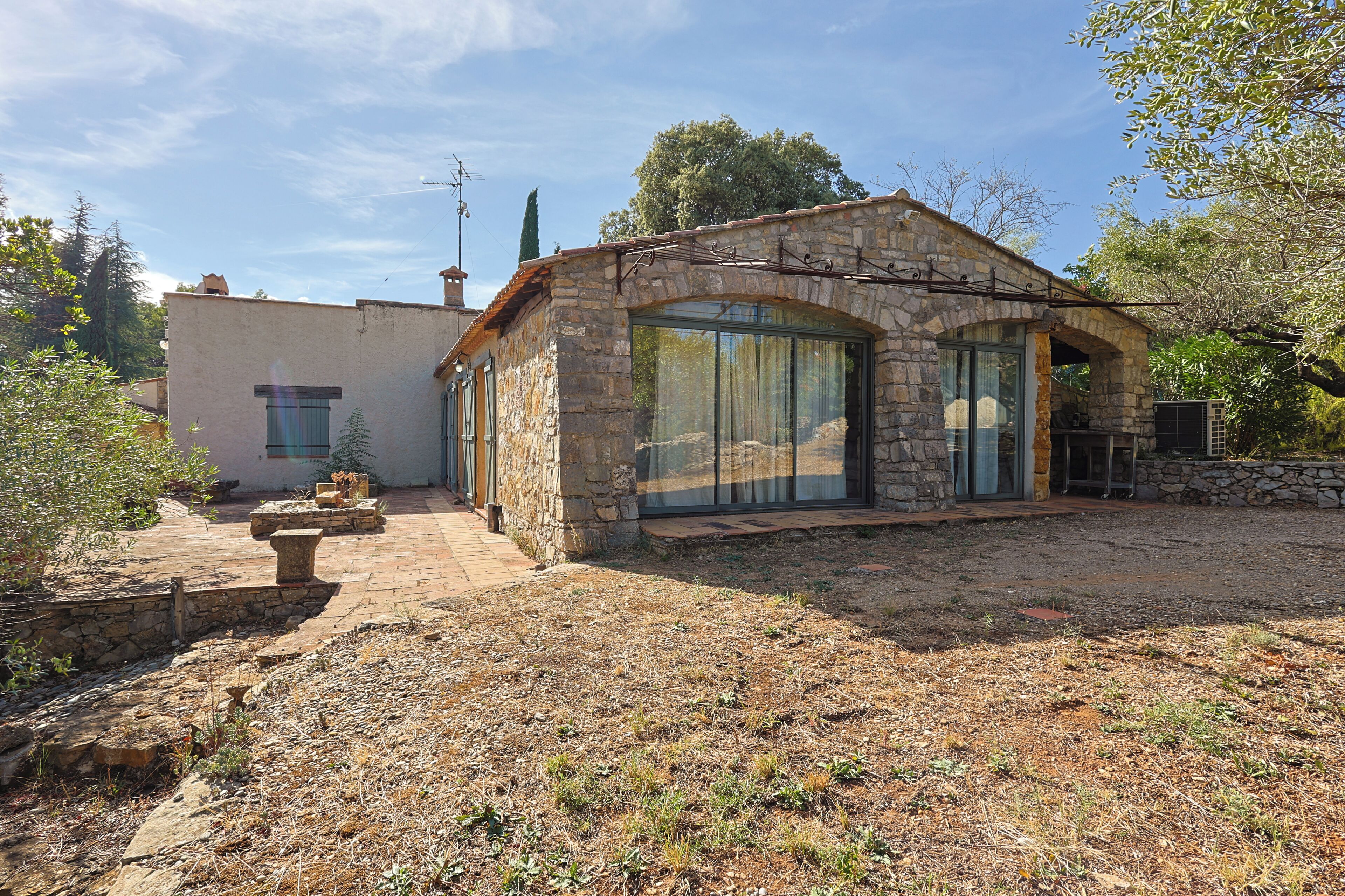 A stone house with a large glass window, a patio area, and a stone wall.