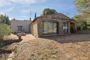 A stone house with a large glass window, a patio area, and a stone wall.