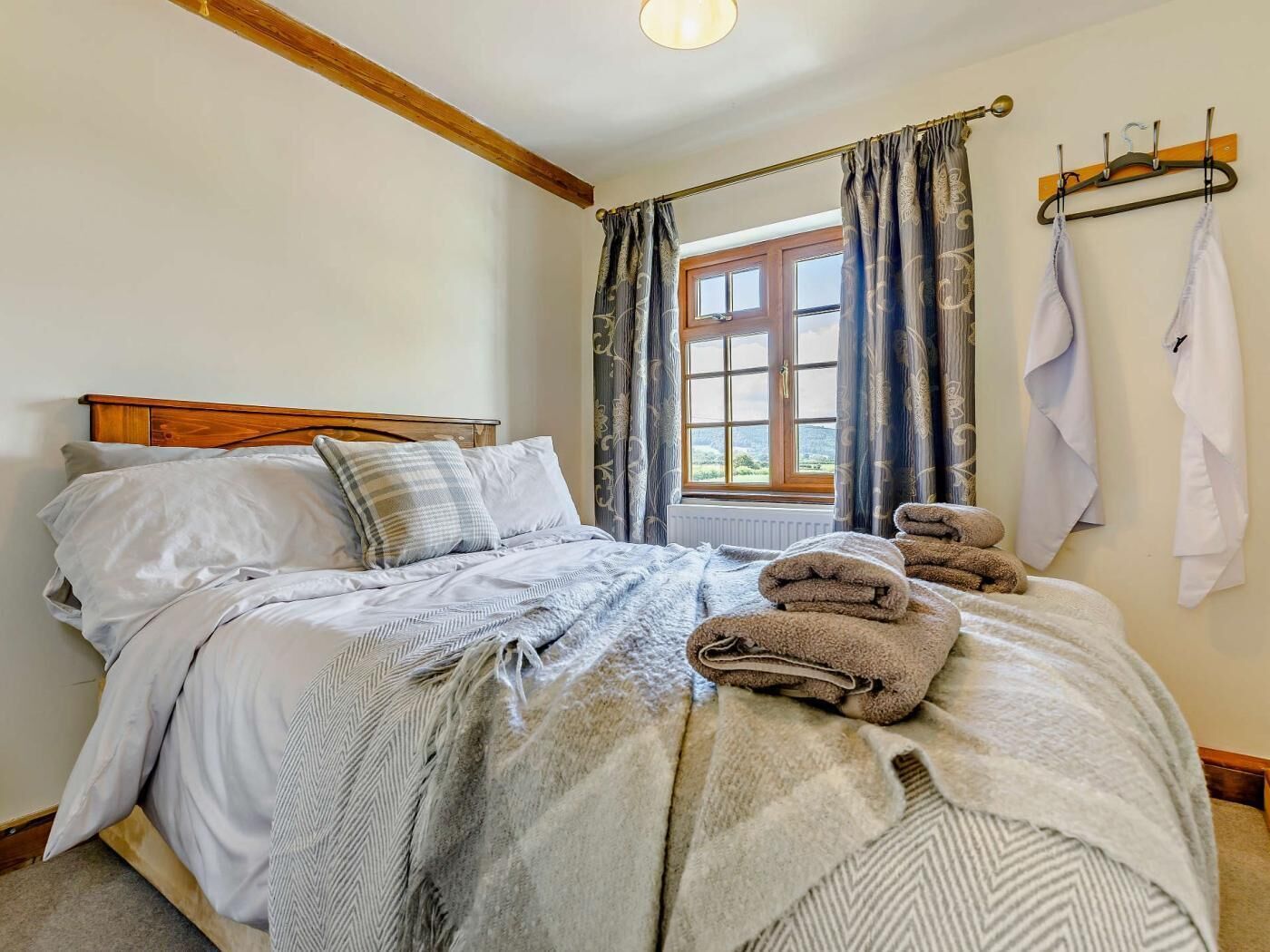 A bed with a wooden headboard, a window with curtains, and a towel rack with towels.