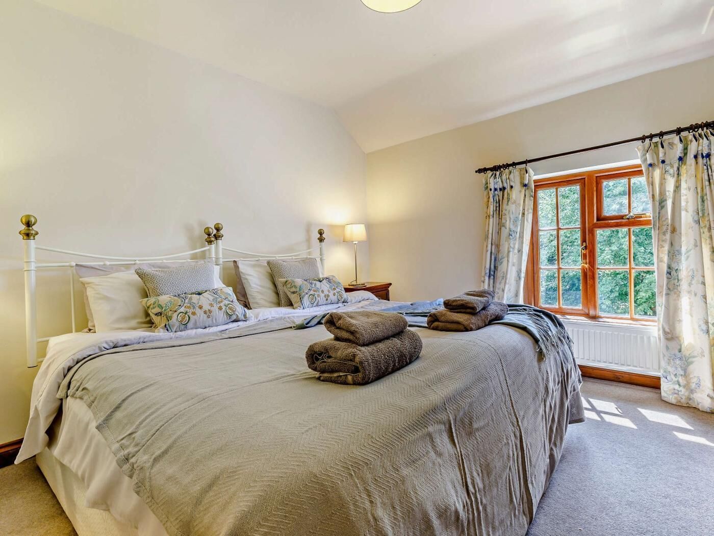 Une chambre à coucher avec un lit, des oreillers, une fenêtre avec des rideaux et un radiateur.