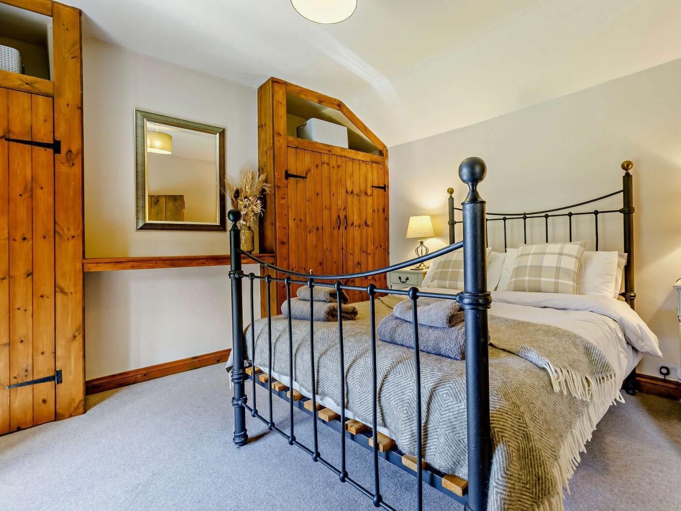 A bedroom with a metal bed frame, wooden wardrobe, and a mirror on the wall.