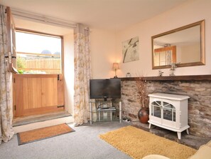 Ein Wohnzimmer mit Fernseher, Kamin und einer Holztür, die in einen Garten führt.