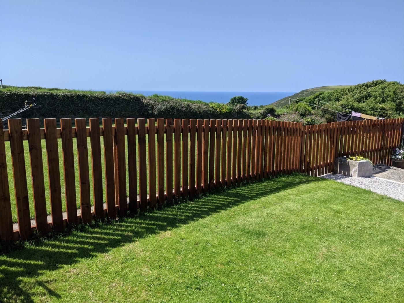 A wooden fence in a well-maintained grassy area with a clear view of the ocean in the background.