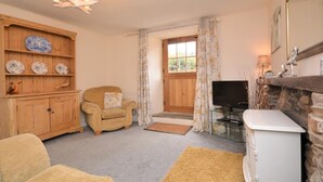 A cozy living room with a wooden cabinet, a comfortable armchair, a television, and a stone fireplace. - 1 Bed in Bude (oc-43697) (Morwenstow)