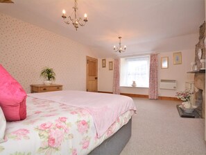 Ein Schlafzimmer mit einem Bett, einer Kandelaber, einem Fenster mit Vorhängen, einer Heizung und einem kleinen Tisch mit einer Pflanze.