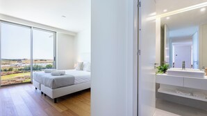 Un dormitorio moderno con una cama grande, un baño con espejo y lavamanos, y vistas al exterior.