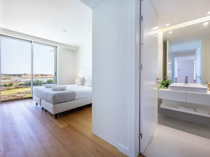 A modern bedroom with a large bed, a bathroom with a mirror and sink, and a view of the outdoors. - Bayline Beach2 - Sea View Apartment in Armação (Armação de Pêra)