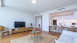 Una sala de estar moderna con televisor de pantalla plana, muebles de madera, un área de cocina y un extintor visible.