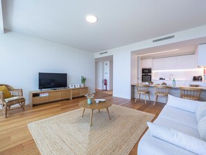 A modern living room with a flat-screen TV, wooden furniture, a kitchen area, and a visible fire extinguisher. - Bayline Beach2 - Sea View Apartment in Armação (Armação de Pêra)