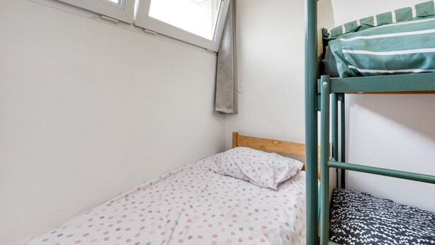 Una cama litera con colcha de lunares y almohada a rayas, una ventana con cortina y cabecera de madera.
