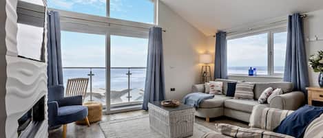 A spacious living room with a large window overlooking the sea, a sofa, a chair, and a small table.