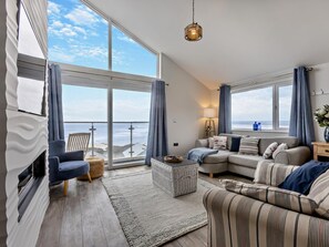 A spacious living room with a large window overlooking the sea, a sofa, a chair, and a small table. - 2 Bed in Bideford (oc-43968) (Westward Ho!)