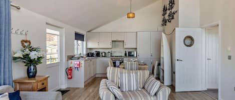 A spacious living area with a sofa, a striped armchair, a kitchen with white cabinets, and a dining table.