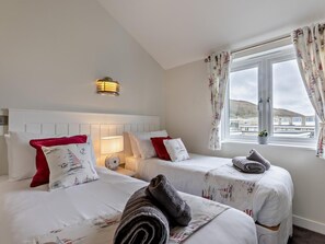 Ein Hotelzimmer mit zwei Betten, einer Nachttischlampe, Meerblick und einem Vorhangfenster.