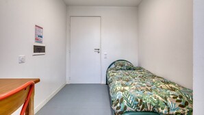 Une petite chambre avec un lit simple, une porte, une petite table et une chaise.