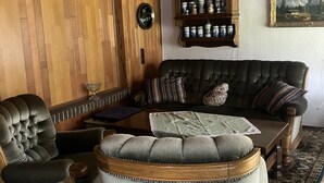 Une pièce de style traditionnel avec un plafond en bois, un canapé, deux fauteuils, une petite table, un meuble contenant des bocaux et un tableau accroché au mur.