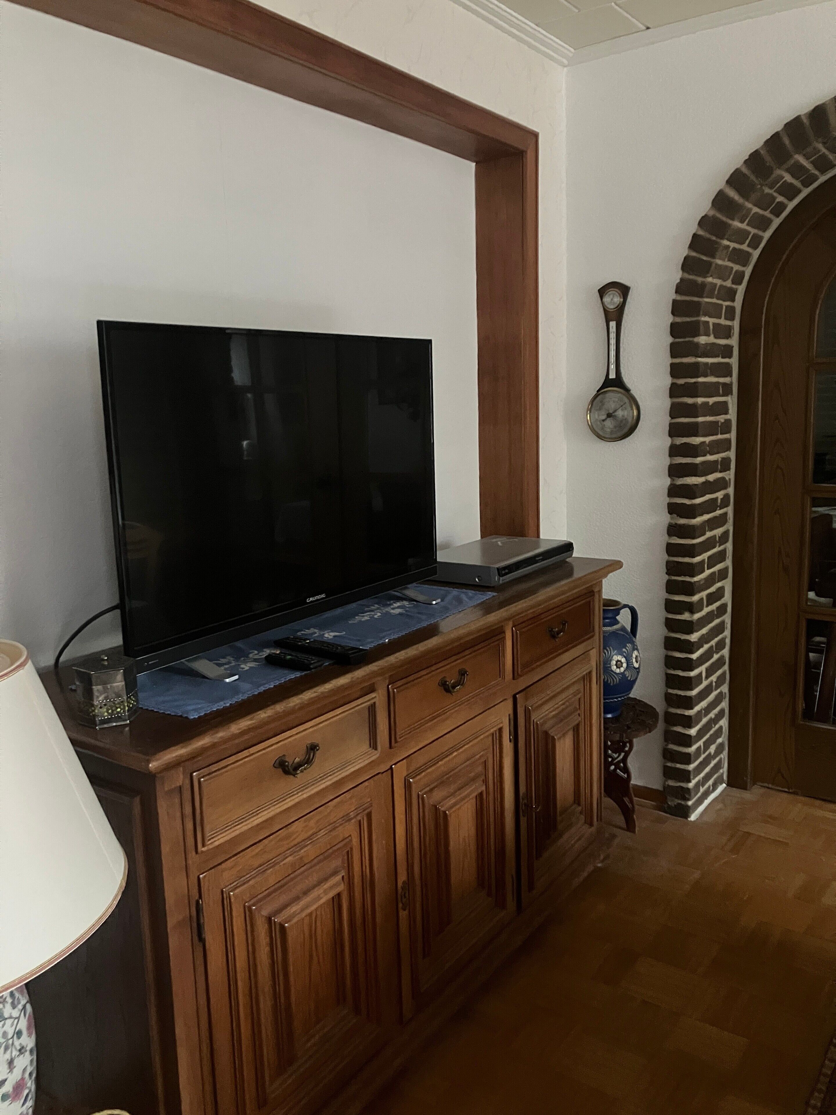 Un televisor de pantalla plana sobre un mueble de madera, un reloj en la pared y una chimenea de ladrillo.