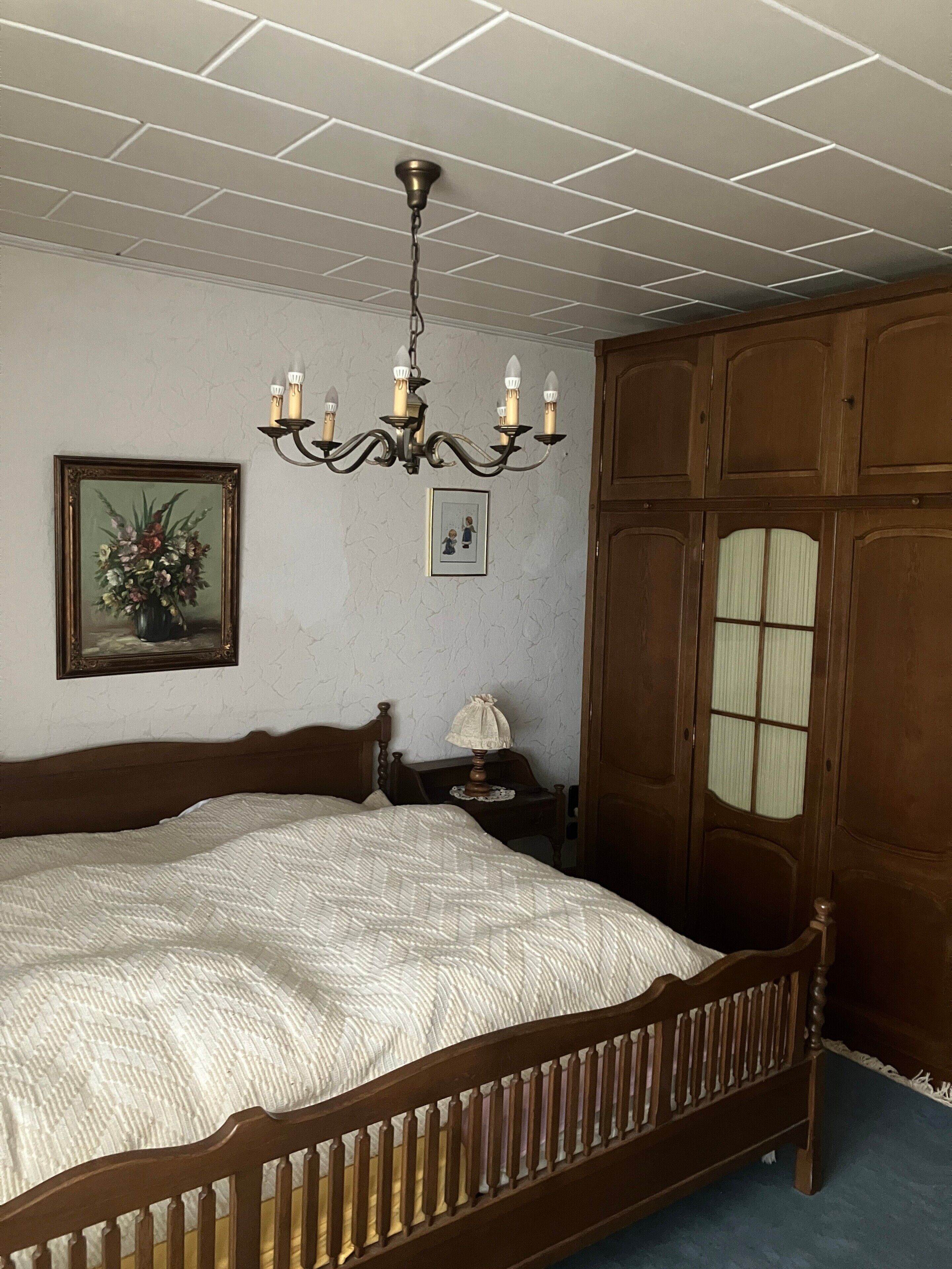 Ein Schlafzimmer mit einem hölzernen Bett, einer Kristalllüster, einem Nachttisch und einem Kleiderschrank.