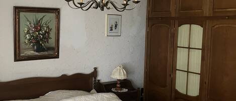 Ein Schlafzimmer mit einem hölzernen Bett, einer Kristalllüster, einem Nachttisch und einem Kleiderschrank.