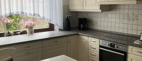 A kitchen with white cabinets, a black countertop, a built-in oven, and a window with sheer curtains.