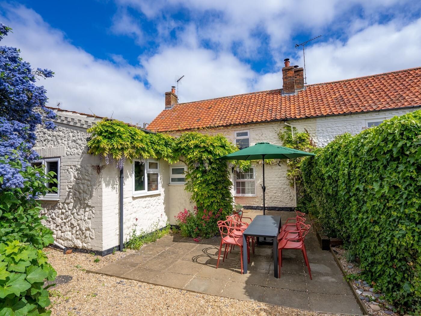 A stone house with a tiled roof, a patio with a table and chairs, and a green umbrella.