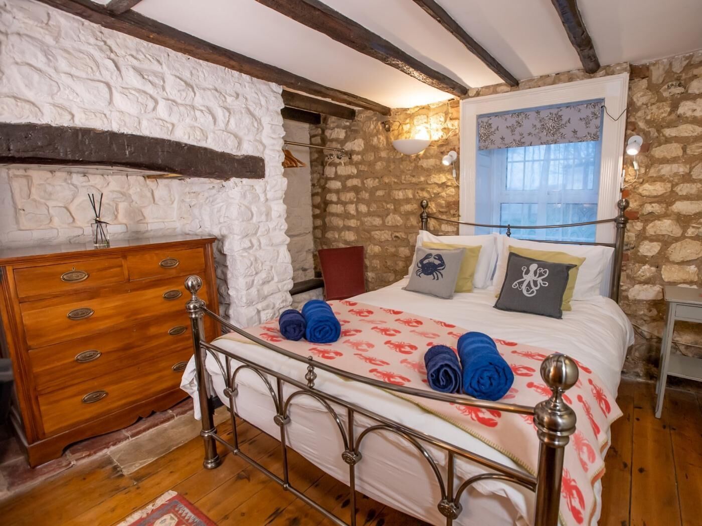 A bedroom with a stone wall, wooden dresser, metal bed frame, and a window with curtains.