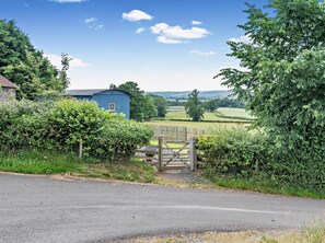 A rural landscape with a blue barn, a wooden gate, and a road.