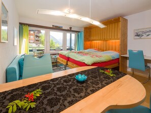 A room with a bed, a desk, a chair, and a view of a mountain landscape. - Silence / Studio Türkis, (Grächen), 1024 by Interhome (Grächen)