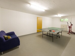 Une pièce avec une table de ping-pong, un canapé bleu avec un coussin, une porte et une fenêtre.