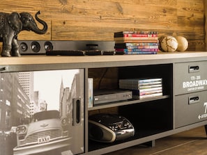 A wooden desk with a stack of books, a small elephant figurine, and a vintage car image on the lower shelf. - Casa Mia Milleggapark, (Grächen), 1095 by Interhome (Grächen)