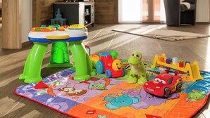 Eine Spielmatte mit Spielzeug und ein kleiner Tisch in einem Raum mit Holzboden und einer Couch.